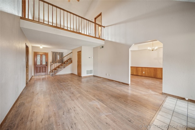 unfurnished living room featuring an inviting chandelier, a high ceiling, and light wood-type flooring