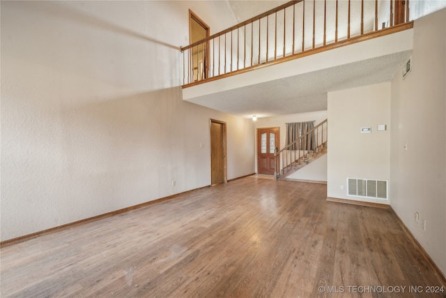 unfurnished living room featuring hardwood / wood-style floors, a textured ceiling, and a high ceiling