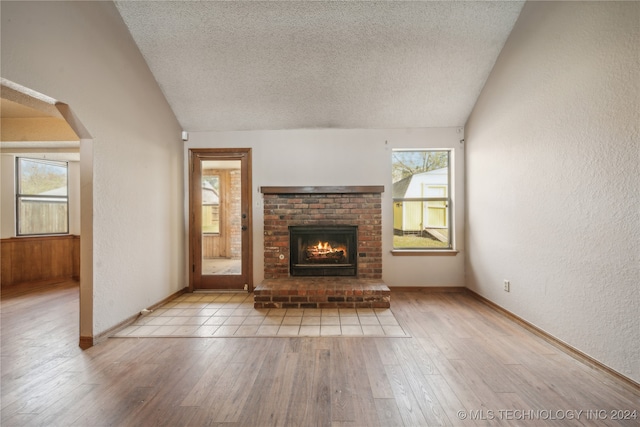 unfurnished living room with light hardwood / wood-style floors, lofted ceiling, and a brick fireplace