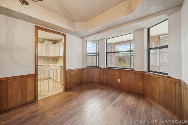 empty room featuring a textured ceiling, hardwood / wood-style flooring, a tray ceiling, and wood walls