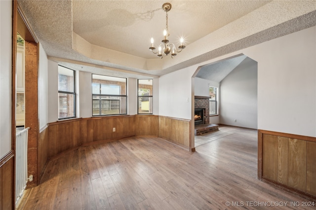 unfurnished dining area featuring wood walls, hardwood / wood-style flooring, a textured ceiling, and a raised ceiling