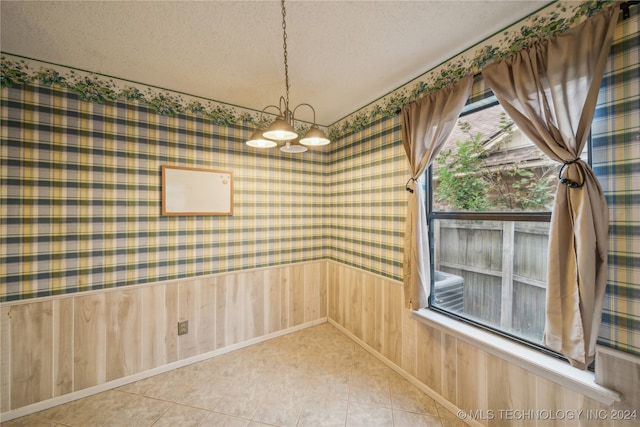 unfurnished room with a notable chandelier, a textured ceiling, and wooden walls