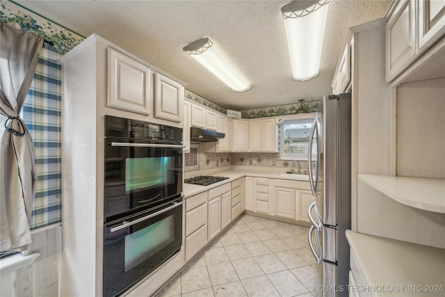 kitchen featuring stainless steel appliances, sink, light tile patterned flooring, a textured ceiling, and tasteful backsplash