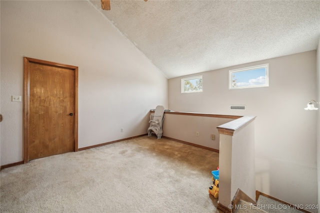 unfurnished room featuring light carpet, a textured ceiling, and vaulted ceiling