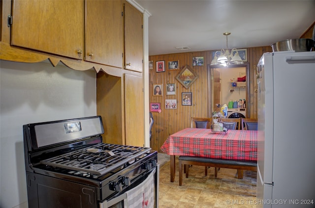 kitchen with wood walls, white refrigerator, decorative light fixtures, black range with gas cooktop, and a chandelier