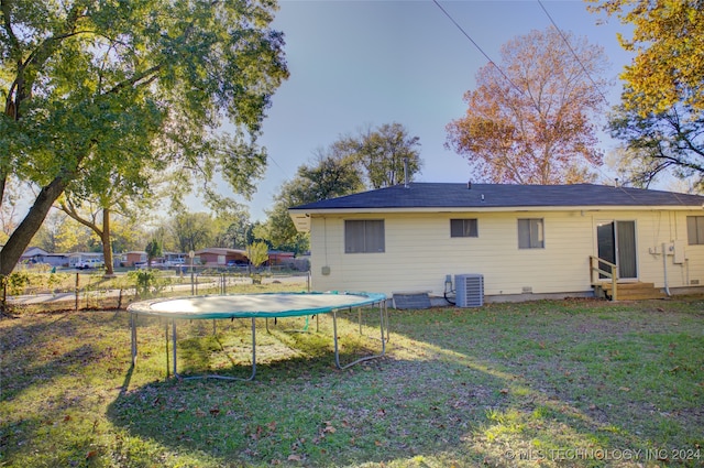 back of property with a lawn, a trampoline, and central air condition unit