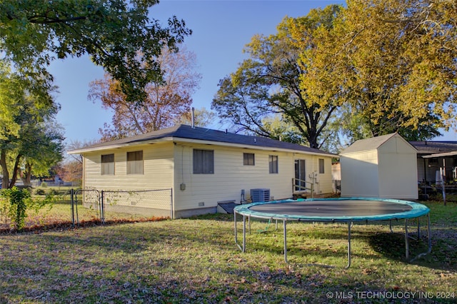 rear view of house with a trampoline, central AC, a storage unit, and a lawn