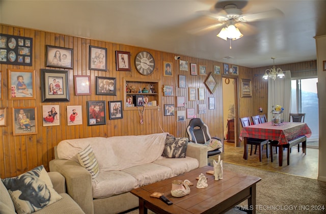 living room with ceiling fan with notable chandelier and wood walls