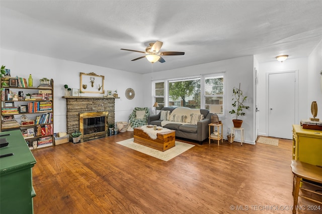 living room with a stone fireplace, wood-type flooring, ceiling fan, and a textured ceiling