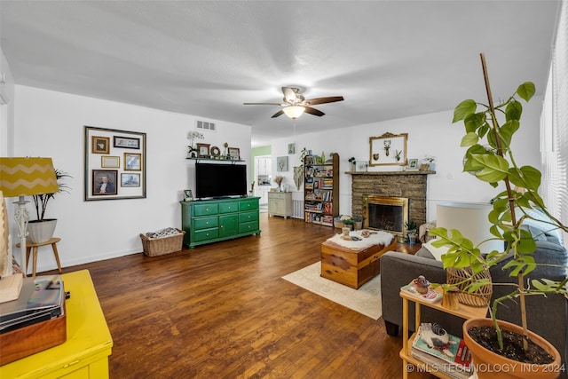 living room featuring dark wood-type flooring, a stone fireplace, and ceiling fan