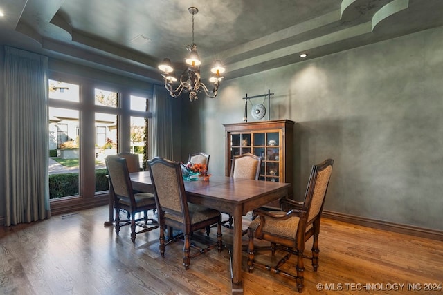 dining area with hardwood / wood-style floors, a raised ceiling, and a chandelier