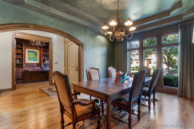 dining area with hardwood / wood-style floors, an inviting chandelier, a raised ceiling, and built in shelves