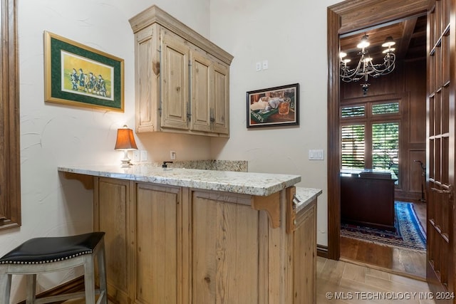 bar featuring light brown cabinetry, light wood-type flooring, an inviting chandelier, and light stone counters