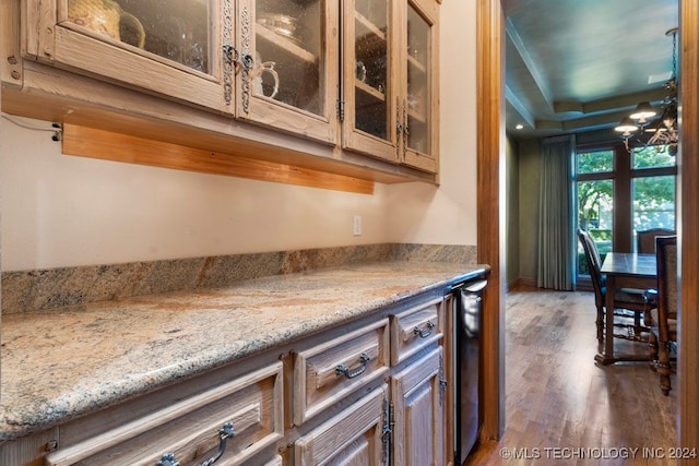 kitchen with dark hardwood / wood-style floors, light stone countertops, a tray ceiling, and an inviting chandelier