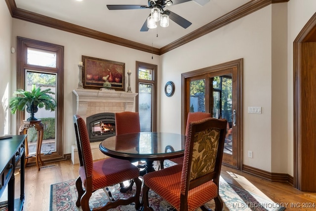 dining room featuring light hardwood / wood-style floors, ornamental molding, a wealth of natural light, and a tiled fireplace