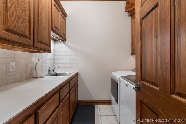 clothes washing area featuring washing machine and dryer, sink, light tile patterned floors, and cabinets