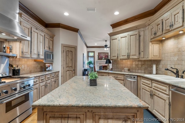 kitchen featuring sink, stainless steel appliances, wall chimney range hood, light stone counters, and a kitchen island