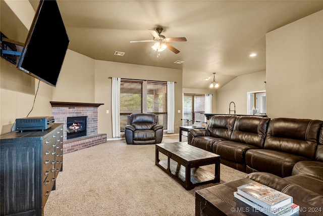 living room with lofted ceiling, a brick fireplace, carpet flooring, and ceiling fan with notable chandelier