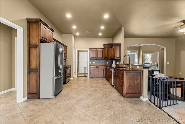 kitchen featuring decorative backsplash, kitchen peninsula, stainless steel appliances, sink, and ceiling fan