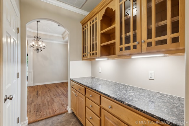 kitchen featuring dark wood-type flooring, hanging light fixtures, dark stone counters, ornamental molding, and an inviting chandelier