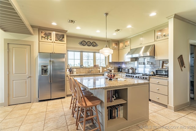 kitchen with appliances with stainless steel finishes, light tile patterned flooring, backsplash, a center island, and light stone counters