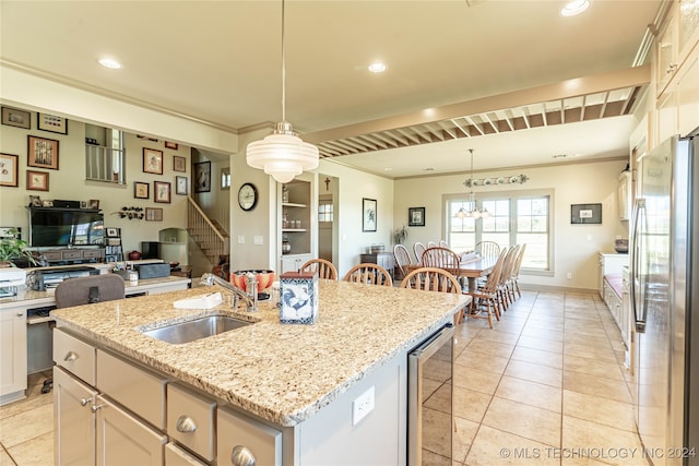 kitchen with beverage cooler, an island with sink, stainless steel refrigerator, sink, and decorative light fixtures