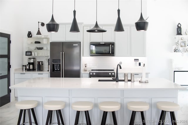 kitchen featuring a kitchen island with sink, a kitchen breakfast bar, stainless steel appliances, decorative light fixtures, and white cabinets