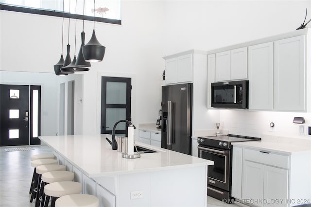 kitchen with black appliances, sink, an island with sink, hanging light fixtures, and white cabinets