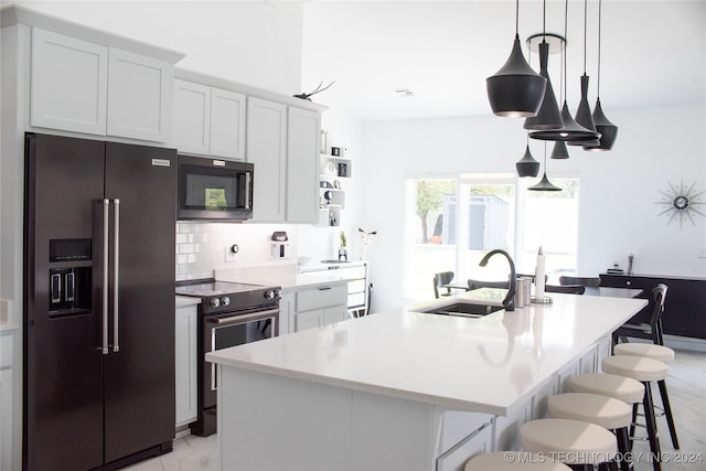 kitchen featuring appliances with stainless steel finishes, white cabinetry, a kitchen island with sink, decorative light fixtures, and sink