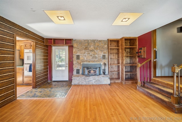 unfurnished living room featuring a textured ceiling, a fireplace, wooden walls, and hardwood / wood-style flooring