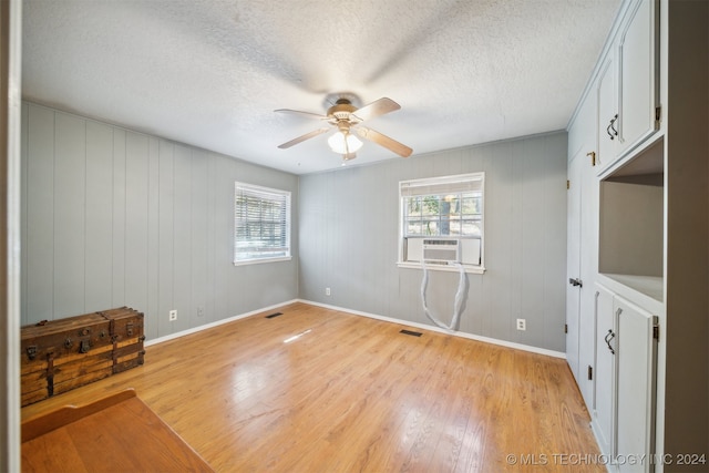 unfurnished room featuring a textured ceiling, light hardwood / wood-style flooring, cooling unit, and ceiling fan