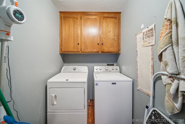 clothes washing area featuring a textured ceiling, cabinets, and washing machine and clothes dryer