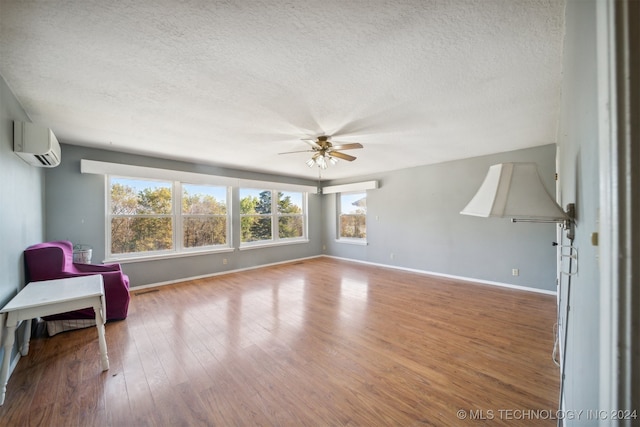 living area featuring ceiling fan, wood-type flooring, a textured ceiling, and an AC wall unit