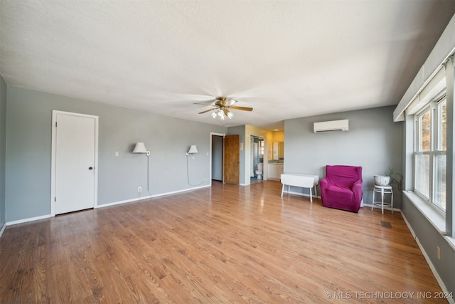 unfurnished room with a wall unit AC, a textured ceiling, ceiling fan, and light hardwood / wood-style flooring