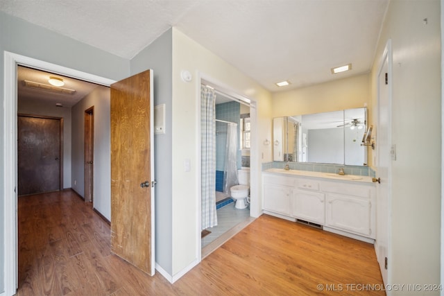 bathroom with toilet, hardwood / wood-style floors, vanity, ceiling fan, and a shower