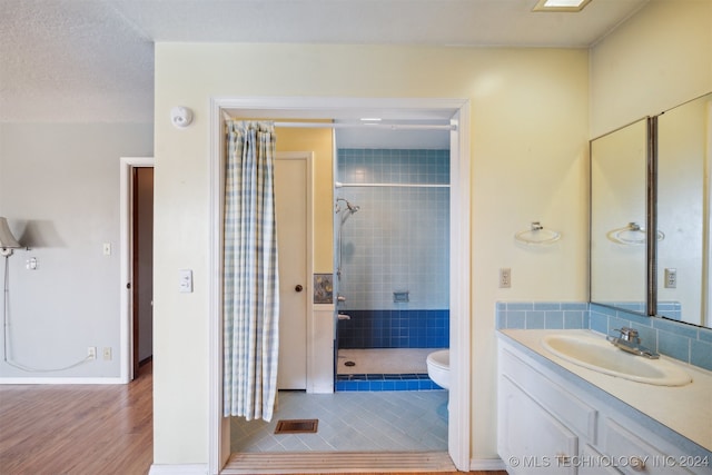 bathroom featuring toilet, vanity, hardwood / wood-style flooring, and tiled shower