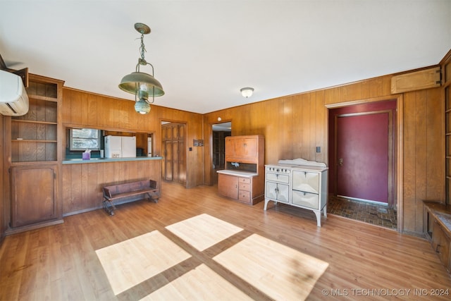 kitchen with a wall mounted AC, kitchen peninsula, wooden walls, white refrigerator with ice dispenser, and light wood-type flooring