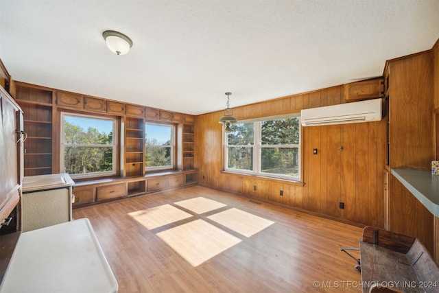 unfurnished dining area featuring a wall unit AC, wooden walls, a textured ceiling, and light hardwood / wood-style floors