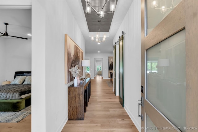 corridor with a barn door, light wood-type flooring, and a chandelier