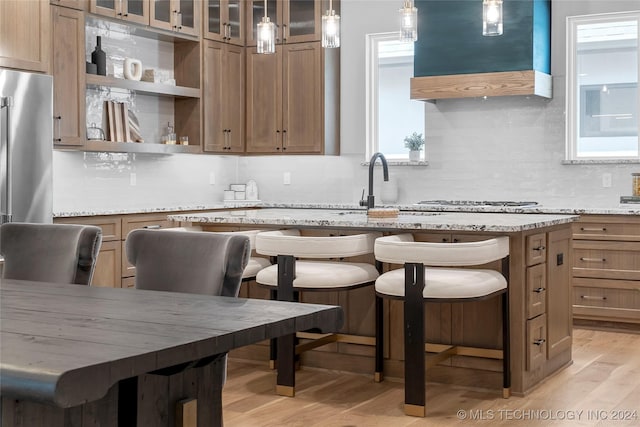 kitchen with a center island, light wood-type flooring, light stone countertops, a breakfast bar area, and extractor fan