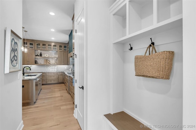 kitchen featuring tasteful backsplash, light stone counters, sink, pendant lighting, and light hardwood / wood-style floors