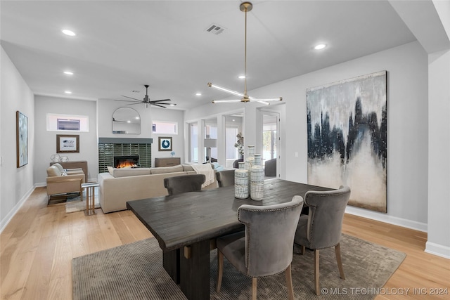 dining space with a tiled fireplace, ceiling fan, and light hardwood / wood-style floors