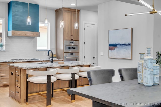 kitchen featuring a kitchen bar, light wood-type flooring, a kitchen island with sink, sink, and hanging light fixtures