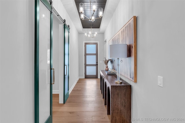 hallway featuring a chandelier, light wood-type flooring, and a barn door