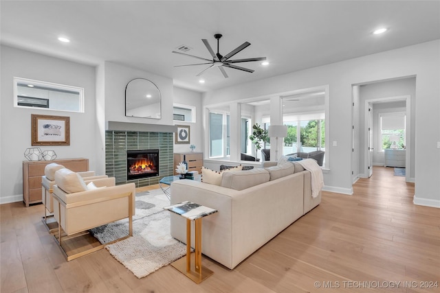 living room featuring a tiled fireplace, ceiling fan, and light hardwood / wood-style flooring