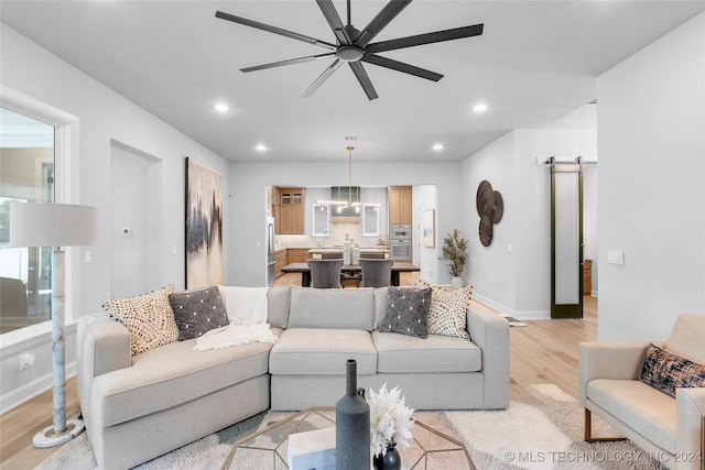 living room with a barn door, light hardwood / wood-style floors, and ceiling fan