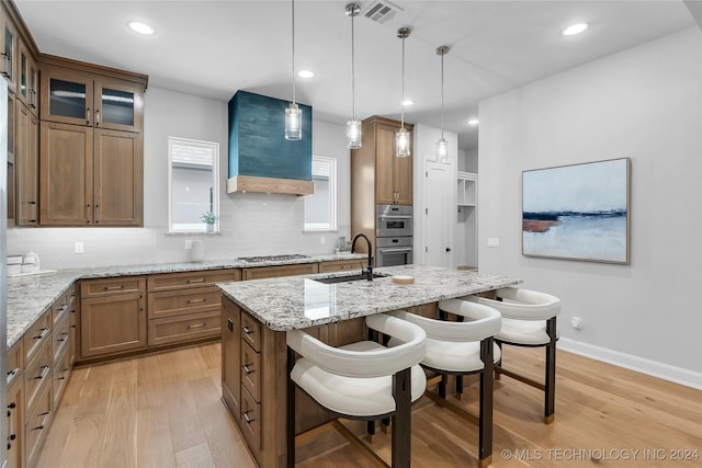 kitchen with a kitchen breakfast bar, light stone counters, sink, pendant lighting, and light hardwood / wood-style flooring