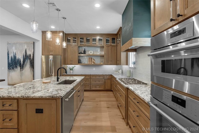 kitchen featuring sink, stainless steel appliances, decorative light fixtures, a kitchen island with sink, and light wood-type flooring