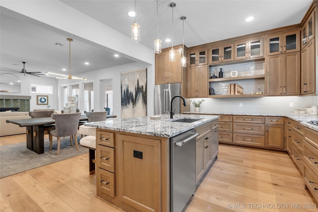 kitchen featuring light wood-type flooring, stainless steel appliances, sink, decorative light fixtures, and a center island with sink