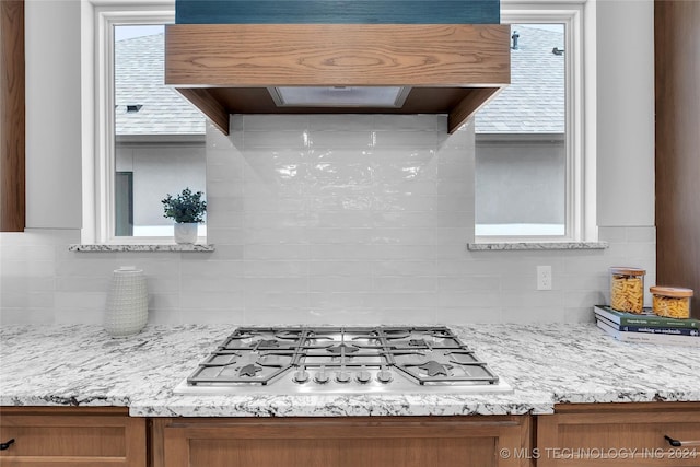 kitchen with stainless steel gas stovetop, light stone countertops, range hood, and tasteful backsplash